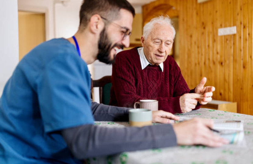 Gentlemen in a red cable knit jumper at a table with an NHS carer