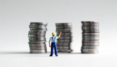 Worker in buke dungarees standing in front of stacks of coins